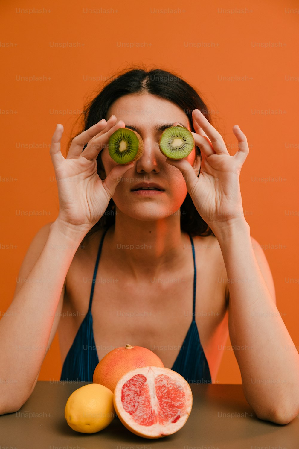 a woman holding two slices of kiwi and a grapefruit