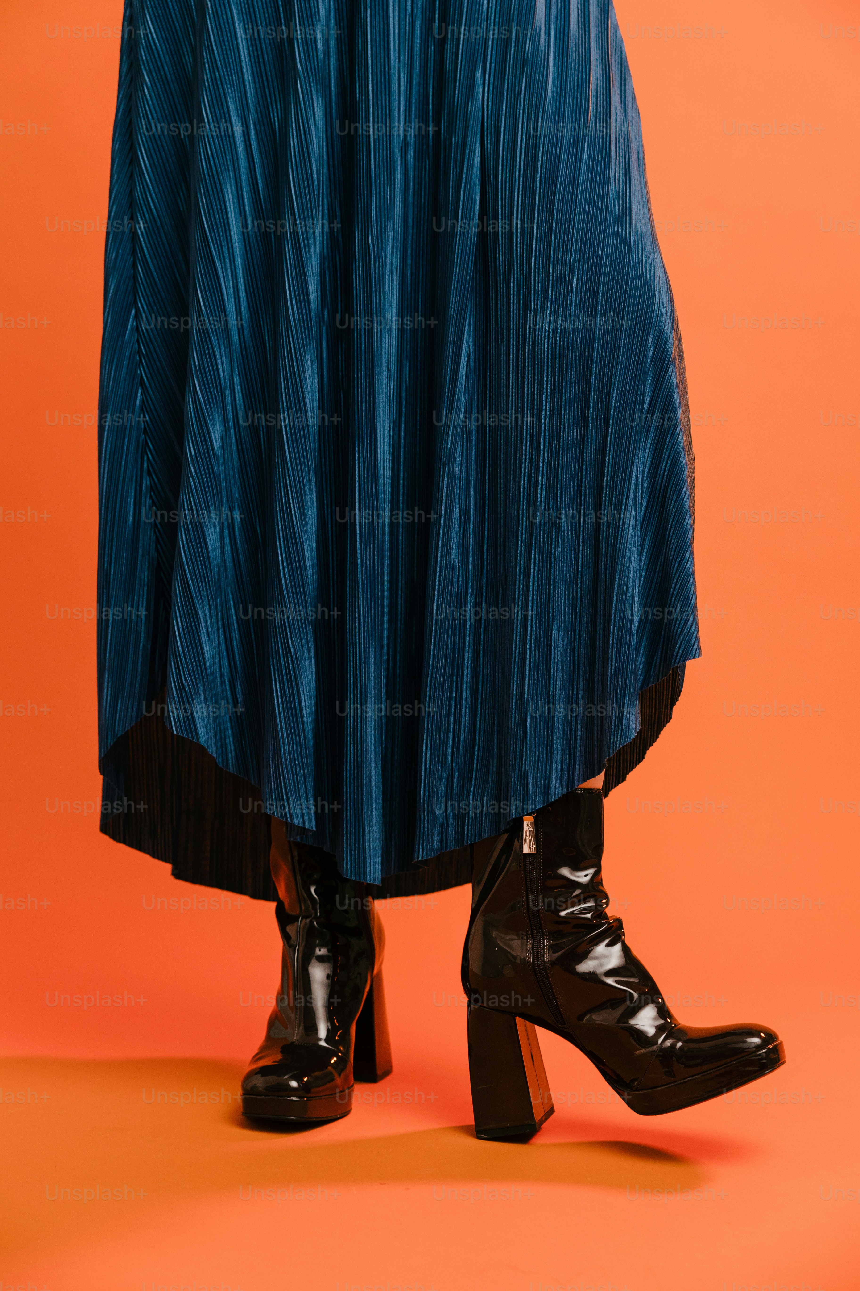 a woman in a blue pleated skirt and black boots