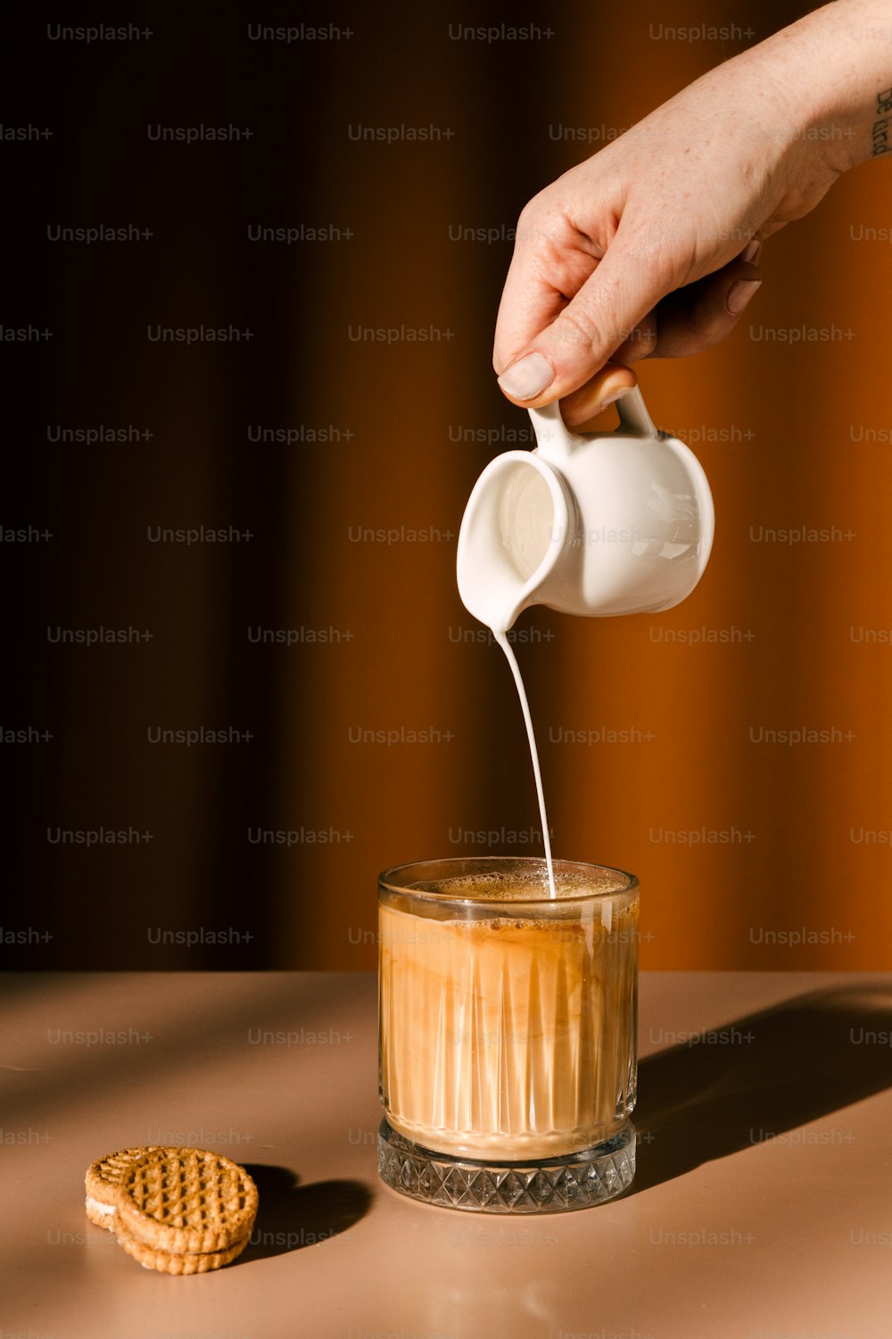 a person pouring tea into a glass with a cookie on the side