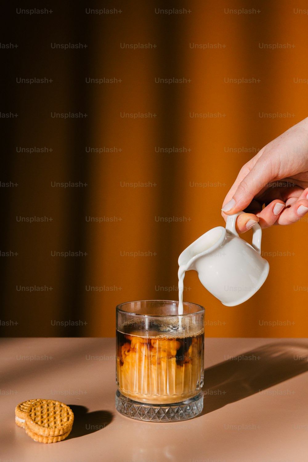 a person pouring tea into a glass with a cookie on the side