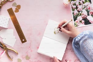 a woman's hand writing on a notebook next to flowers