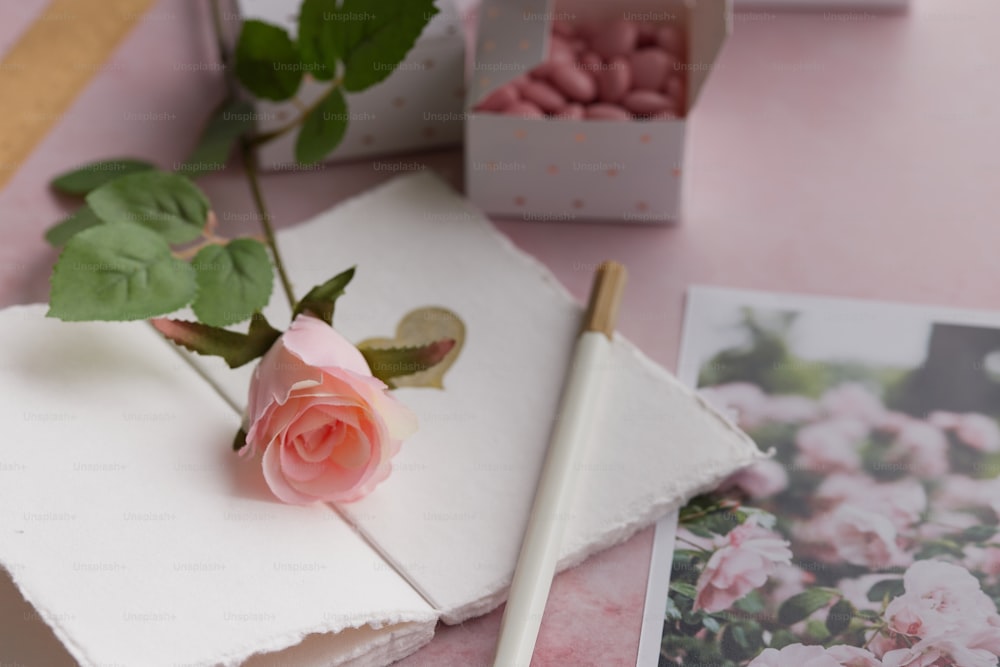 Una rosa rosa sentada encima de una mesa junto a una caja de macaro