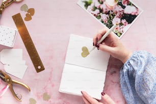 Die Hand einer Frau schreibt auf einem Notizblock neben einem rosa Tisch mit