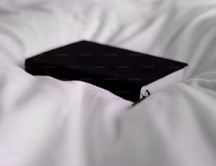 Un libro negro sentado encima de una cama blanca
