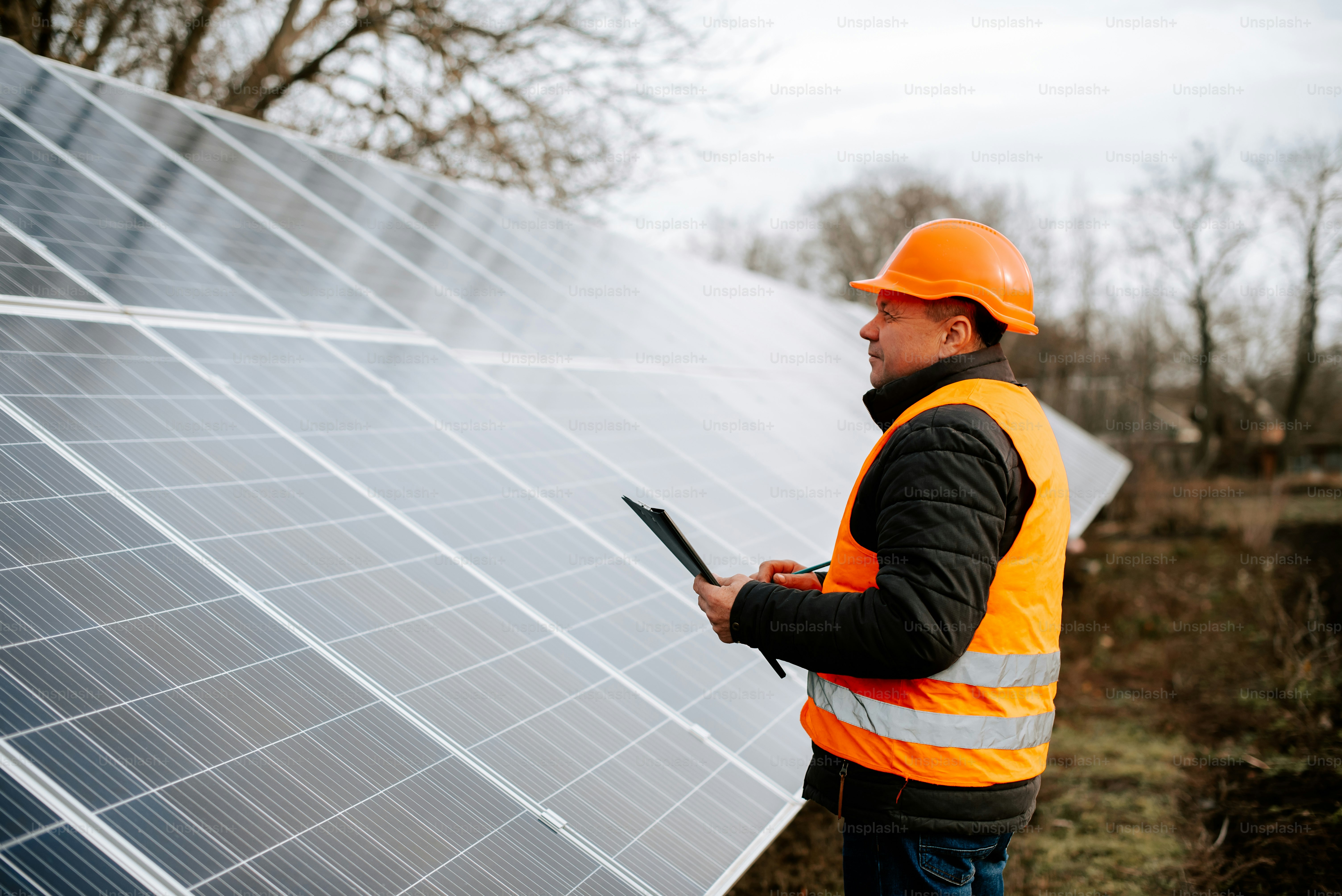 Ein Mann in orangefarbener Weste und Schutzhelm steht neben einem Solarpanel