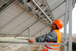 Ein Mann in orangefarbener Warnweste und Schutzhelm steht in der Nähe eines Solarpanels