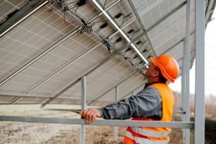Un uomo con un giubbotto di sicurezza arancione e un elmetto rigido è in piedi vicino a un pannello solare