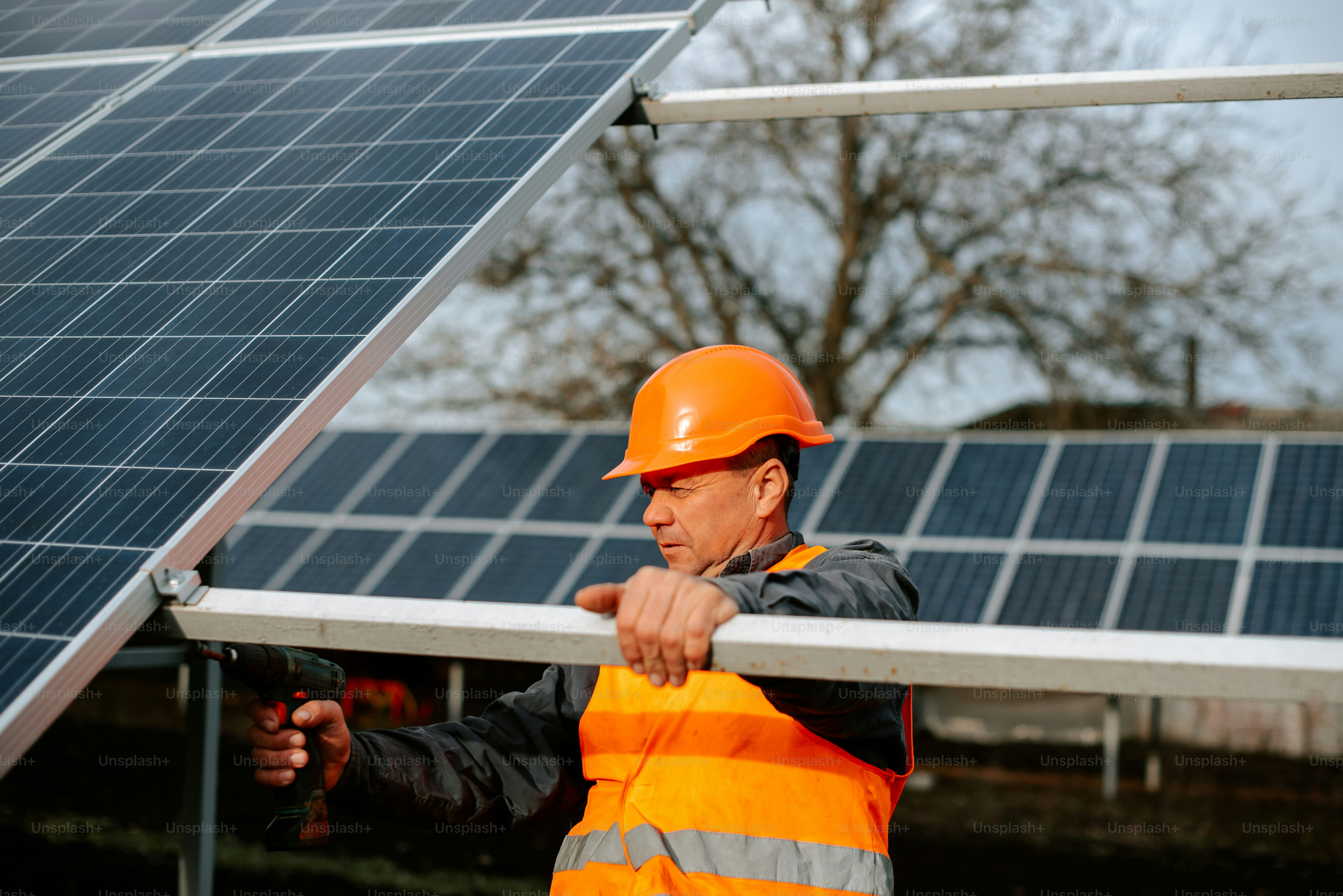 Ein Mann in orangefarbener Sicherheitsweste und Schutzhelm hält eine Schiene in der Nähe einer Solaranlage