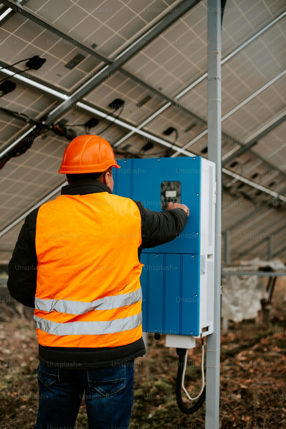 Un hombre con un chaleco de seguridad naranja está arreglando un panel solar