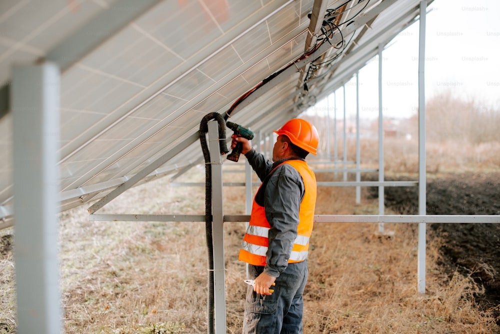 Un hombre con un chaleco de seguridad naranja está arreglando un panel solar