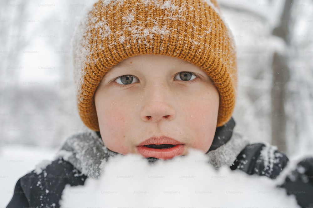 a young boy wearing a hat and blowing snow