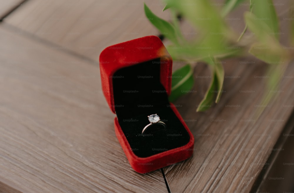 una caja de anillo de terciopelo rojo con un diamante blanco en ella