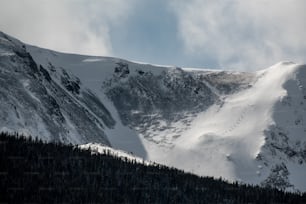 Ein Berg mit Schnee und Bäumen bedeckt unter einem bewölkten Himmel