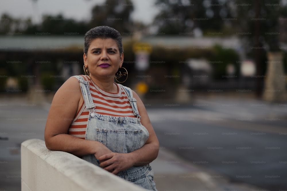 a woman in overalls leaning against a wall