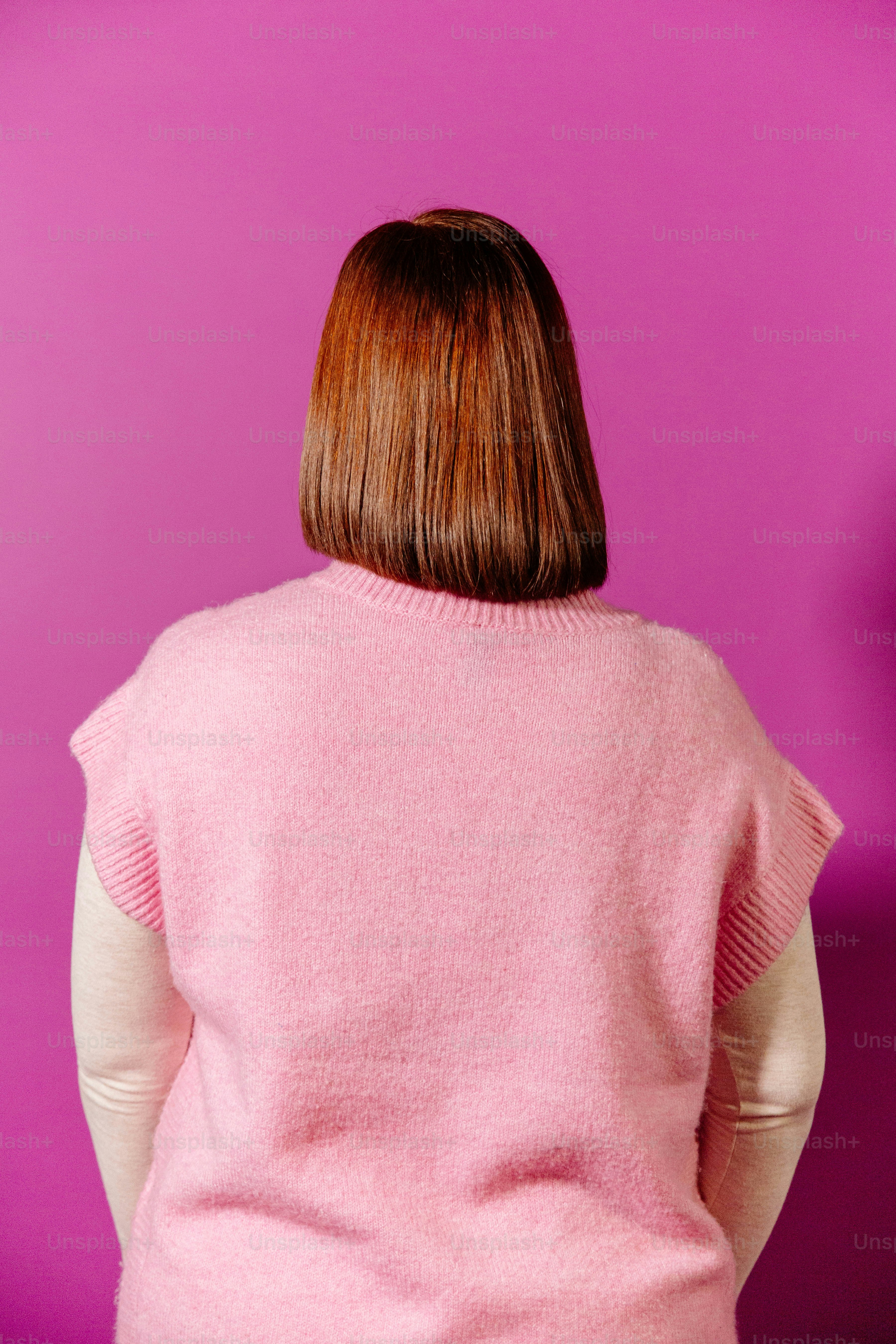 Una mujer con un suéter rosa de pie contra una pared púrpura