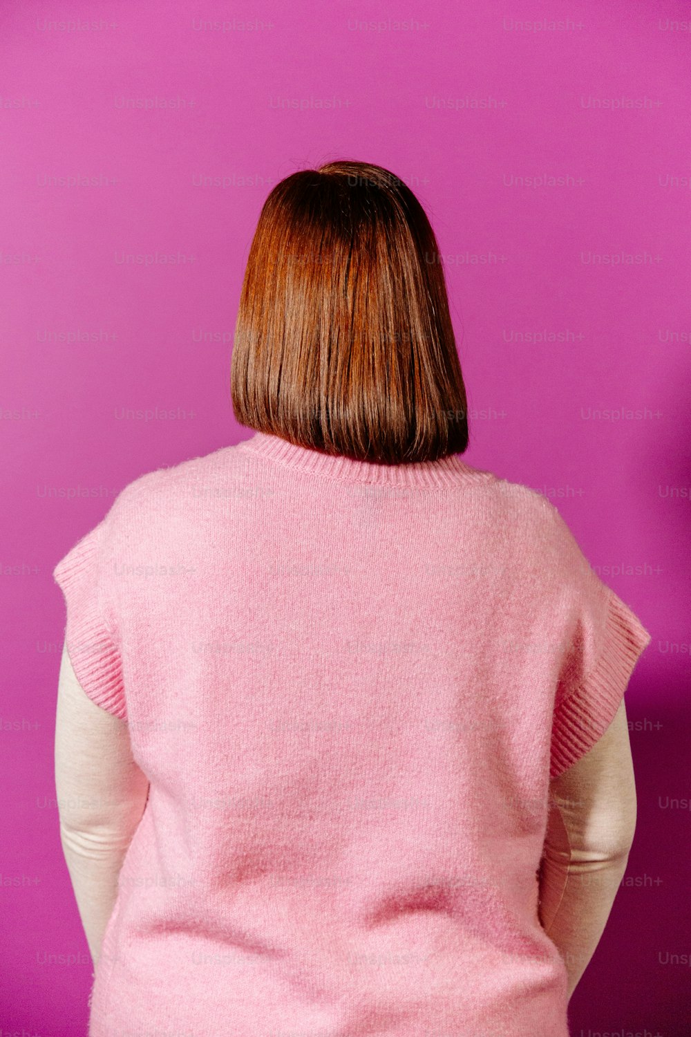a woman in a pink sweater standing against a purple wall