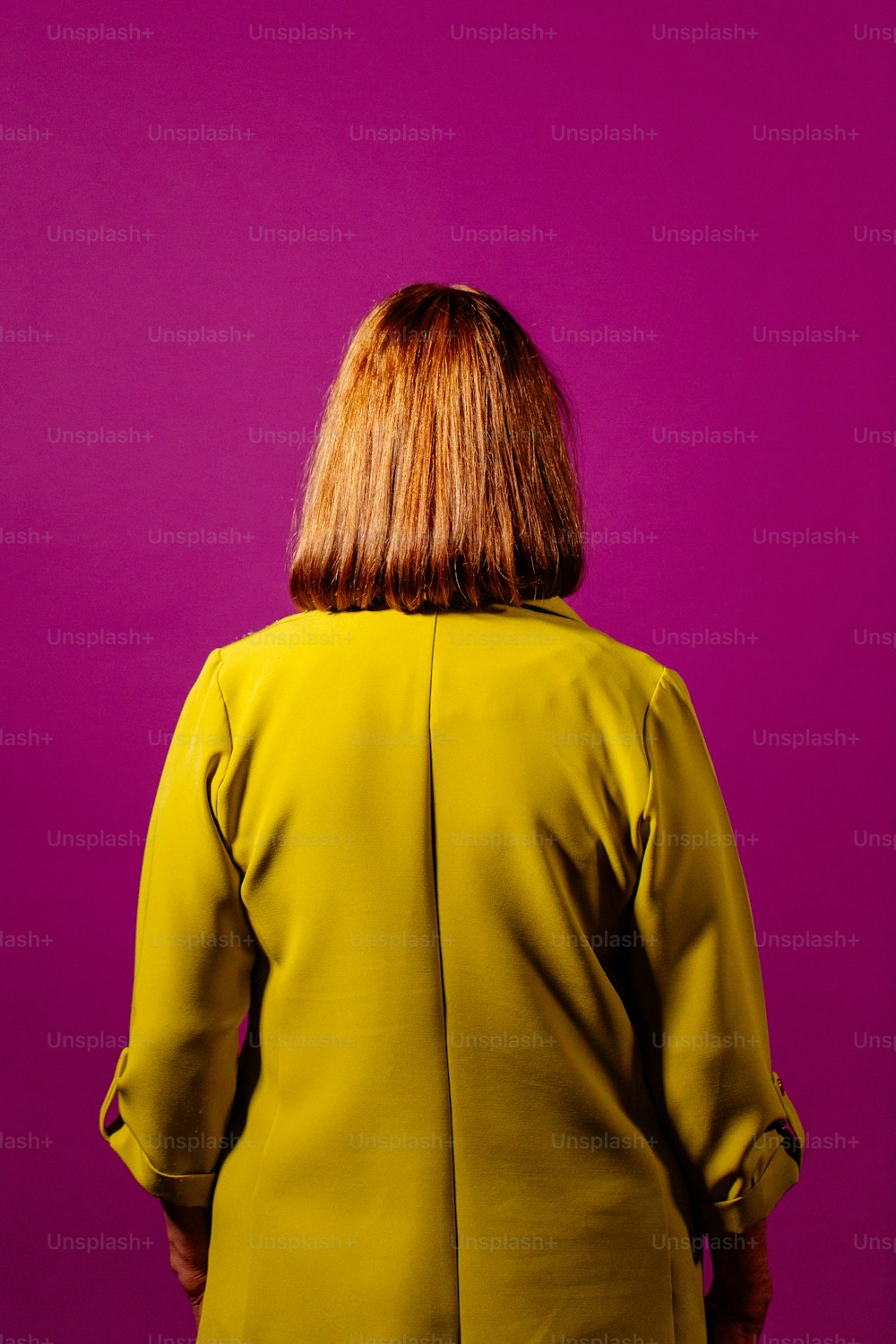 die Rückseite der gelben Jacke einer Frau vor violettem Hintergrund