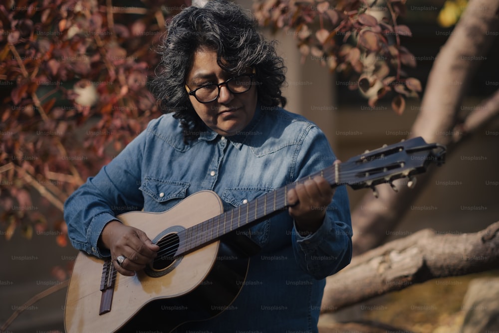 a woman playing a guitar in front of a tree