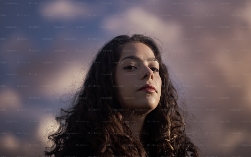 a woman with long hair standing in front of a cloudy sky