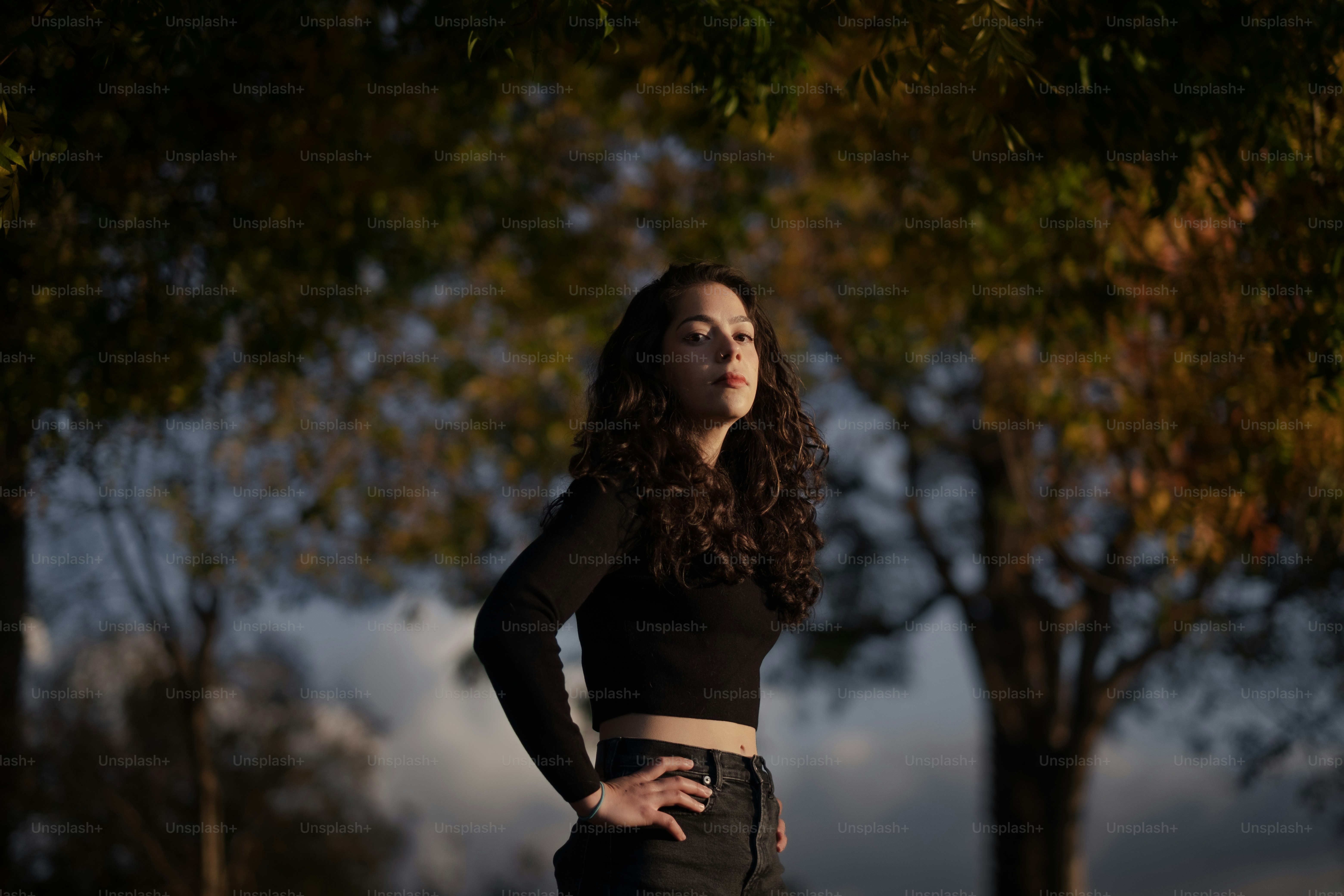a woman standing in front of trees with her hands on her hips