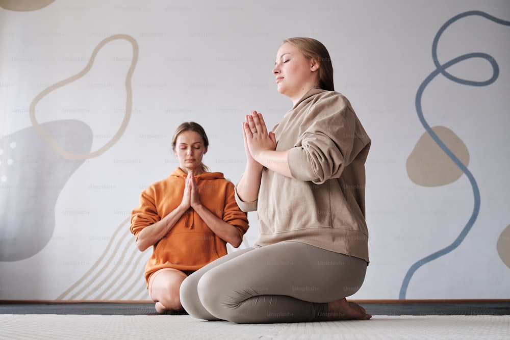 a woman sitting on the ground in front of a woman in a yoga pose