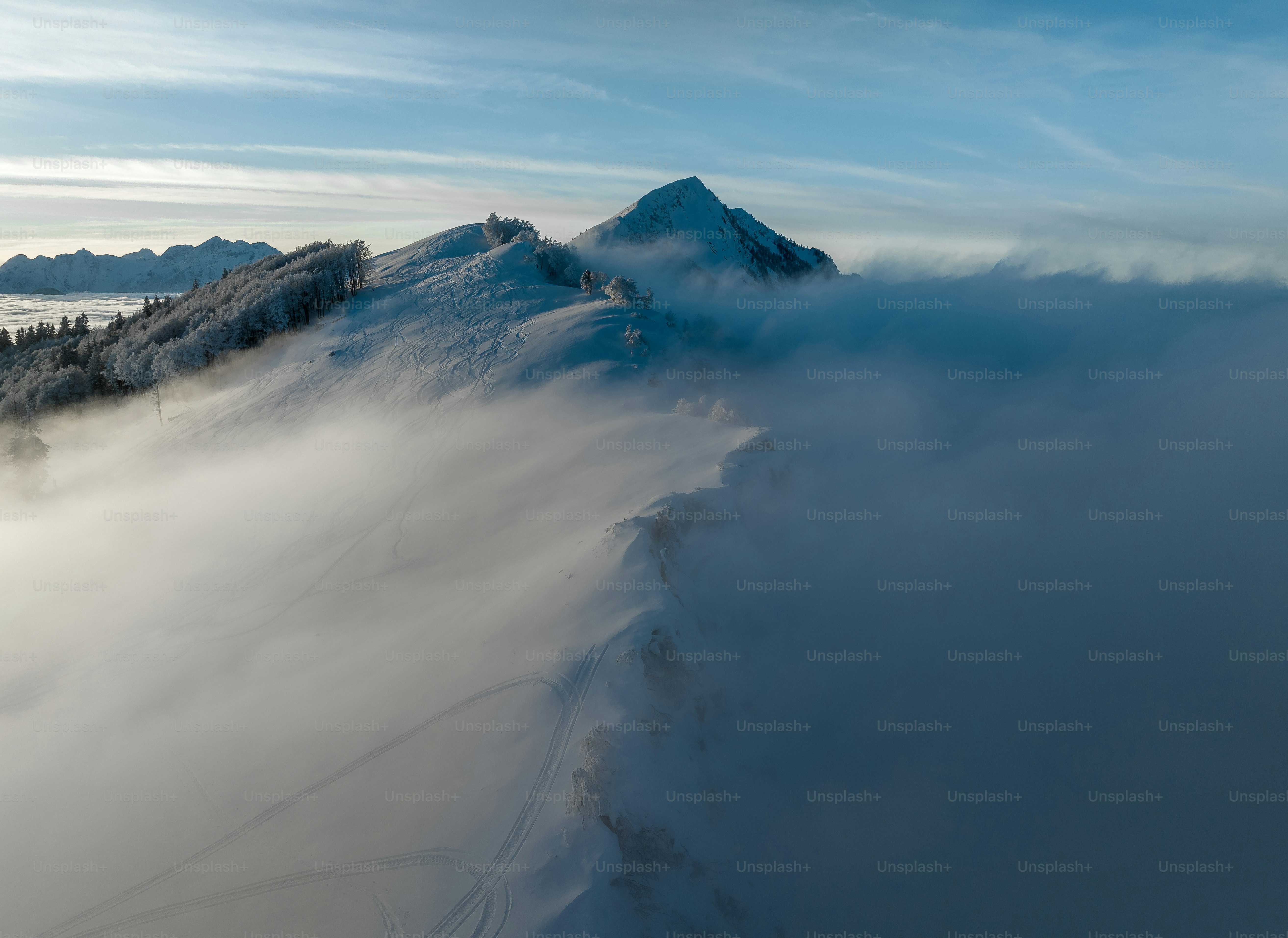 a mountain covered in snow and clouds under a blue sky