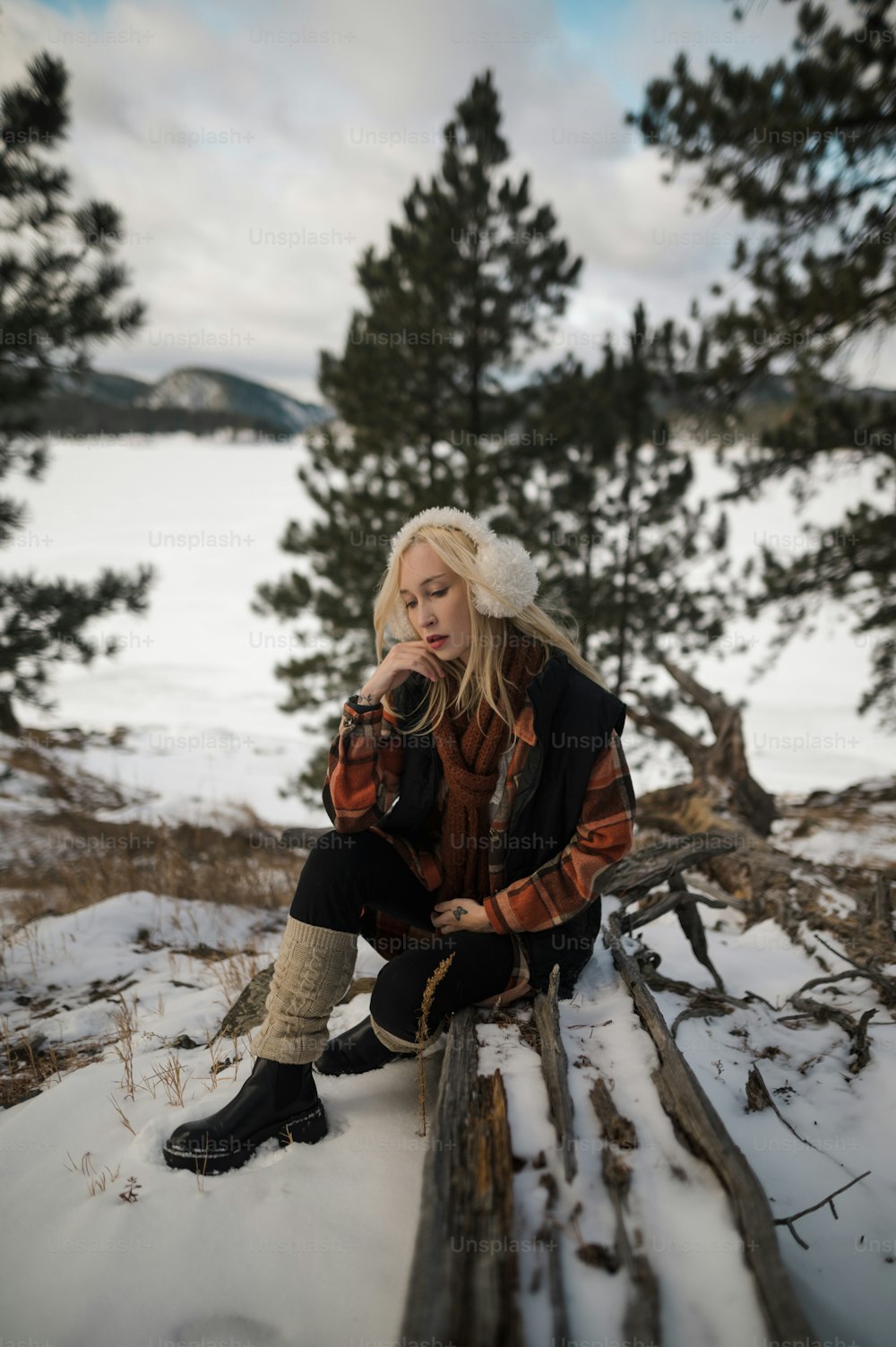 uma mulher sentada em um tronco na neve