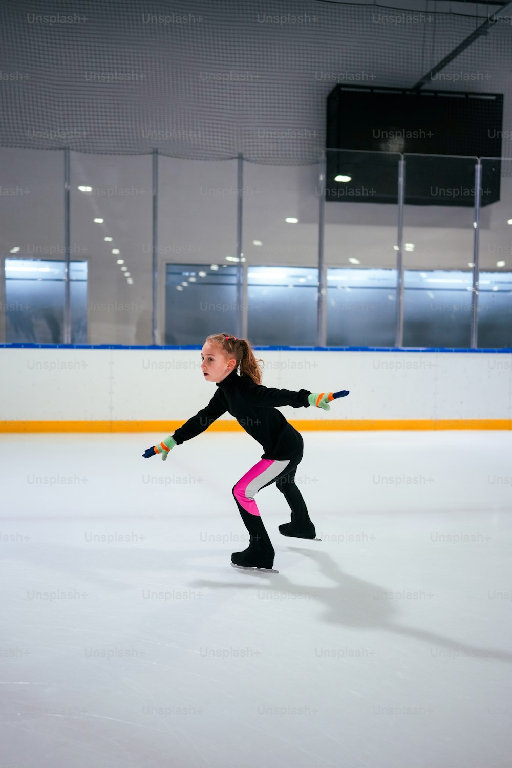 Niña practicando patinaje artístico en una pista de hielo cubierta