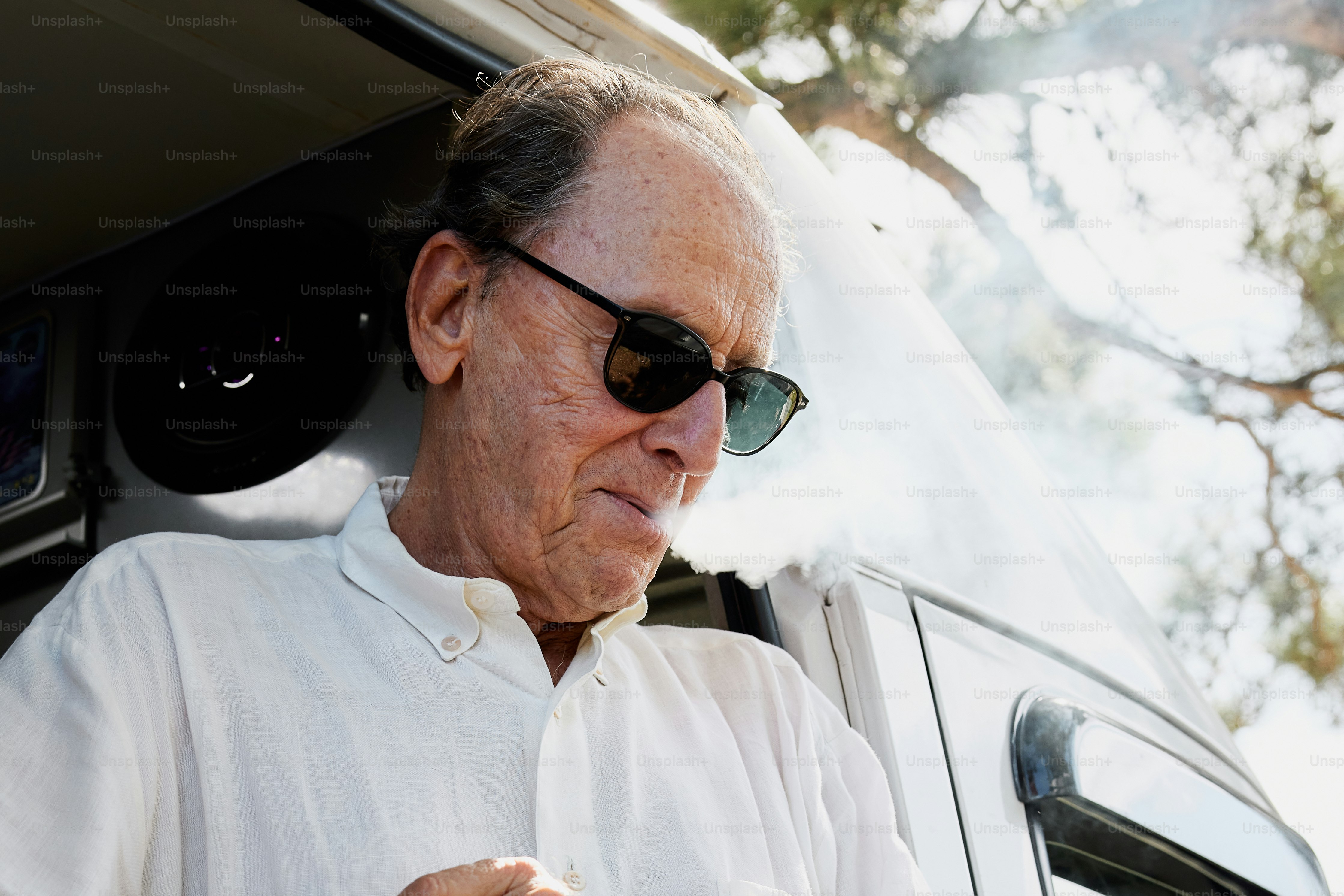 Un hombre con gafas de sol fumando un cigarrillo frente a un coche