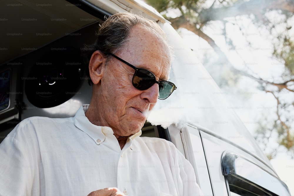 a man in sunglasses smoking a cigarette in front of a car