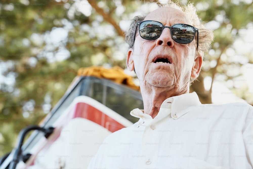 um homem mais velho usando óculos escuros em pé na frente de um ônibus