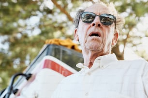 an older man wearing sunglasses standing in front of a bus