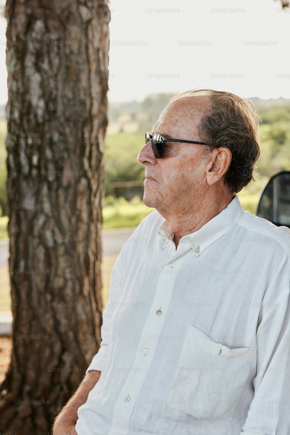 a man wearing sunglasses sitting next to a tree