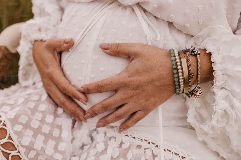a pregnant woman wearing bracelets and a white dress
