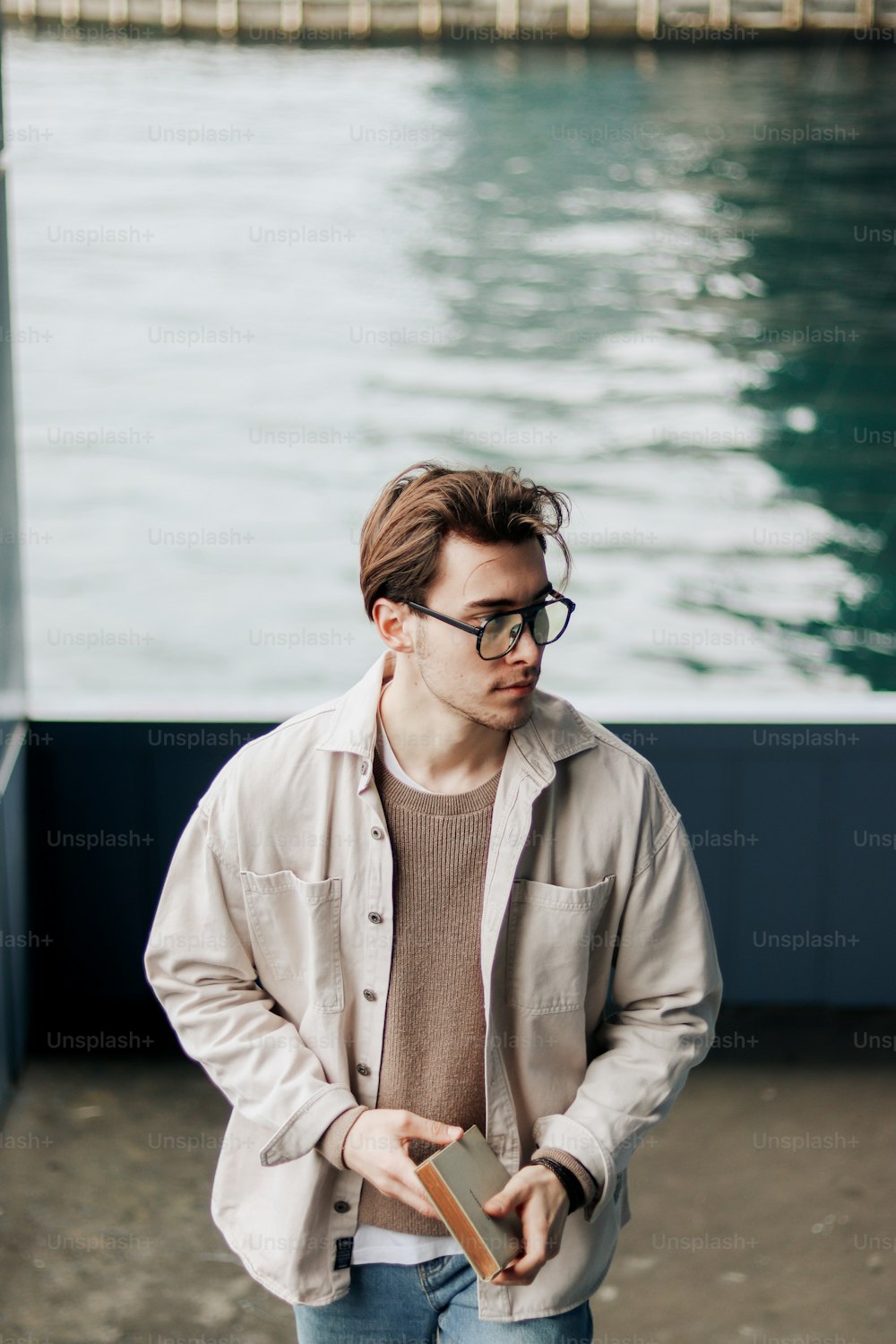 a man with glasses standing next to a body of water