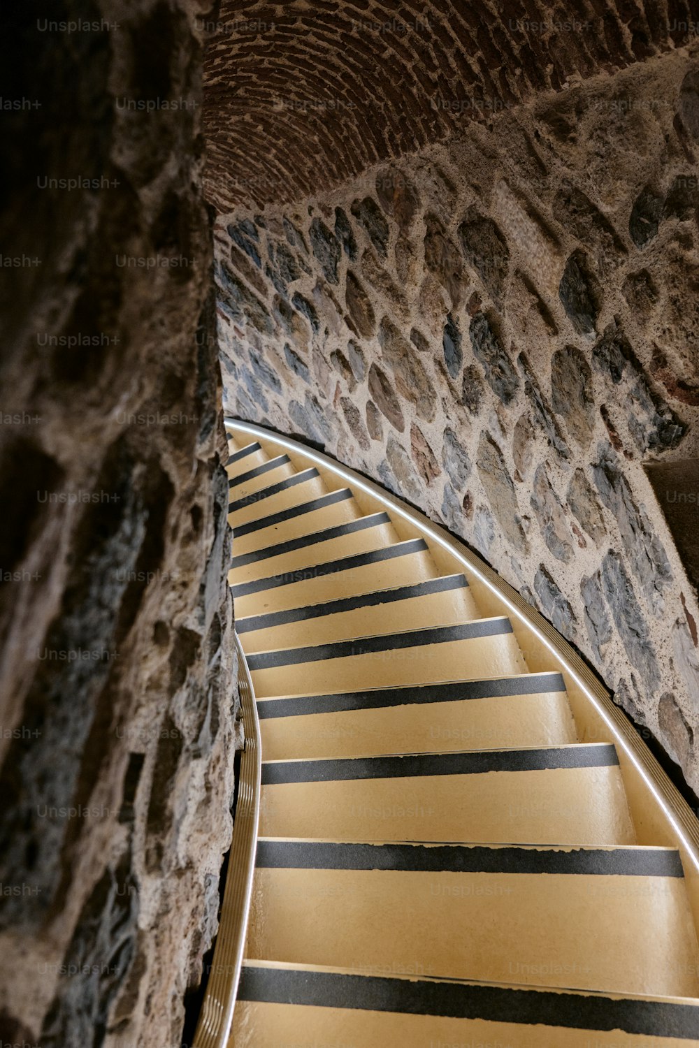 a yellow and black striped stair case next to a stone wall