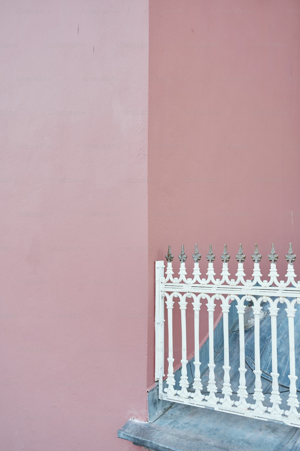 a white iron fence against a pink wall