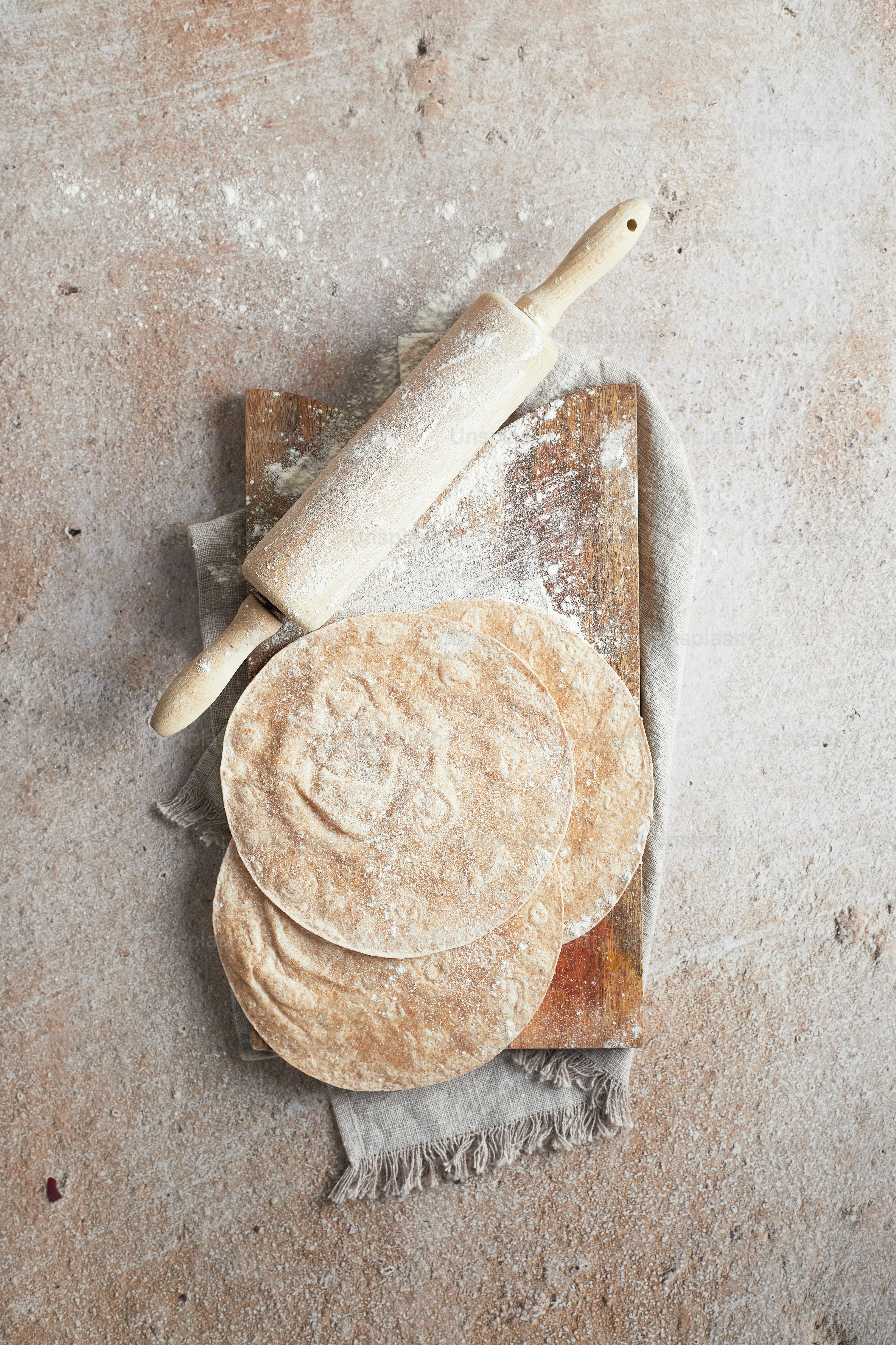 a wooden cutting board topped with three uncooked pizza crusts