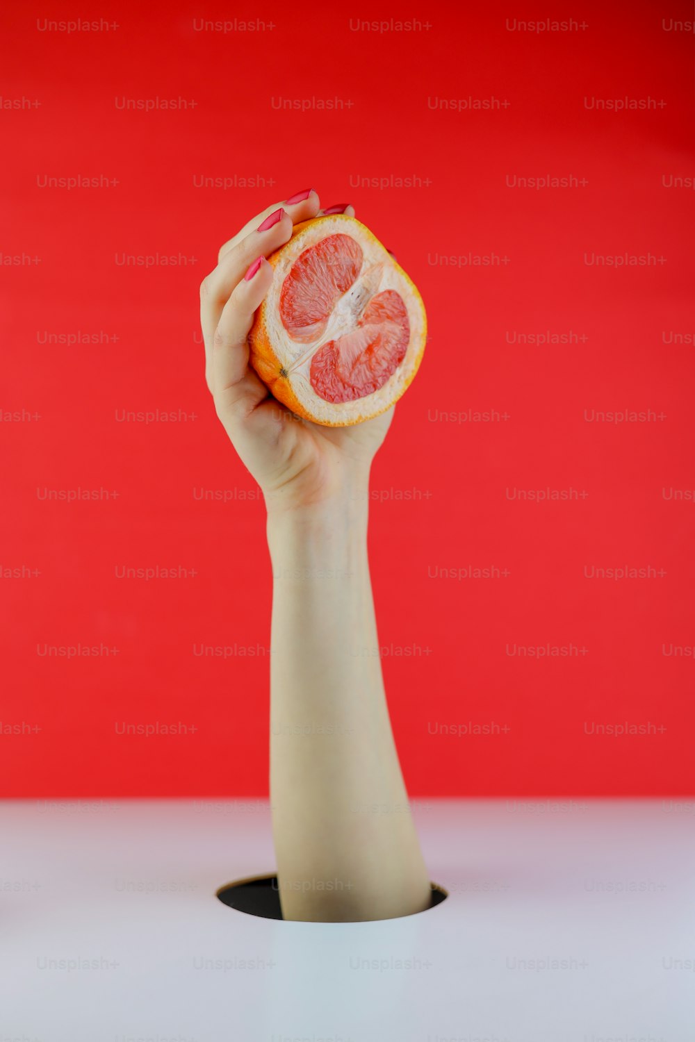a hand holding a grapefruit in front of a red background