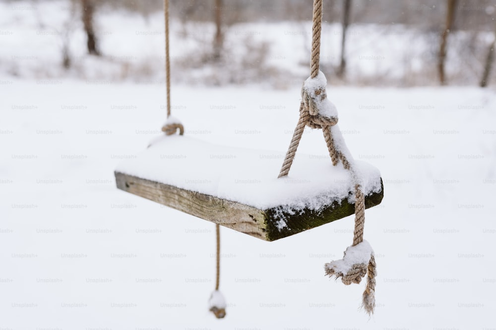 eine schneebedeckte Holzschaukel, die an einem Seil hängt