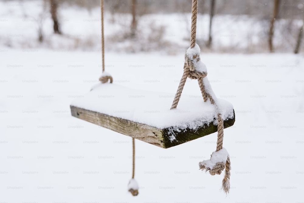 a snow covered wooden swing hanging from a rope