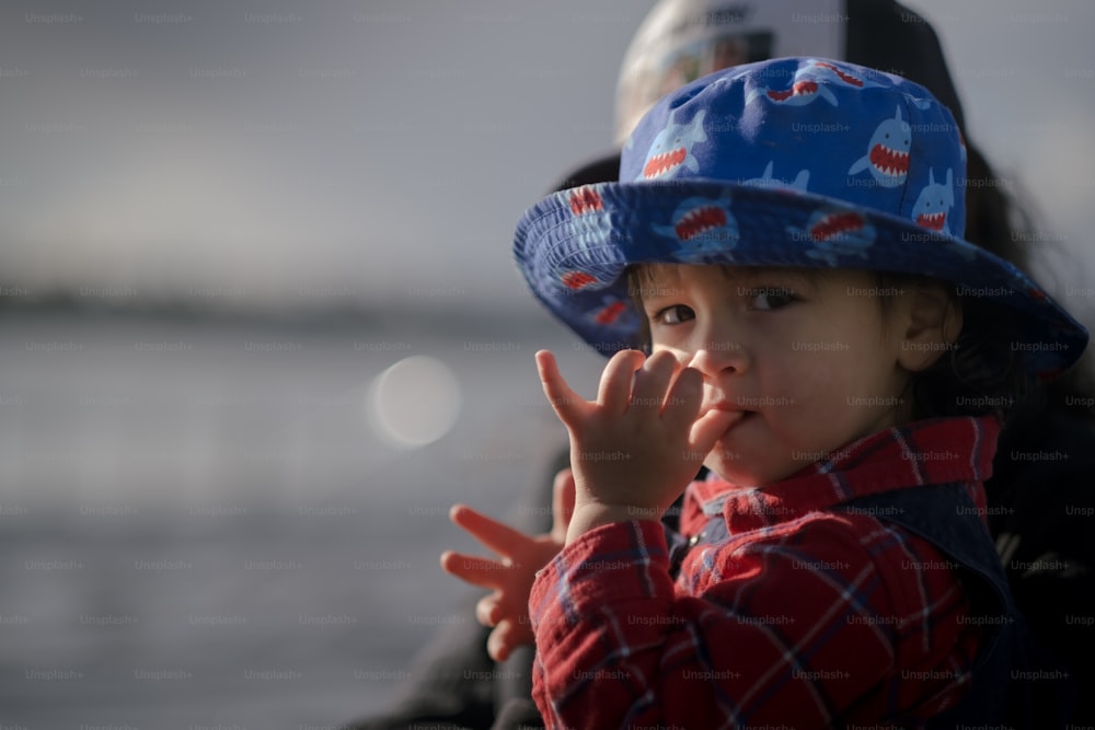 a small child wearing a blue hat and making a hand gesture