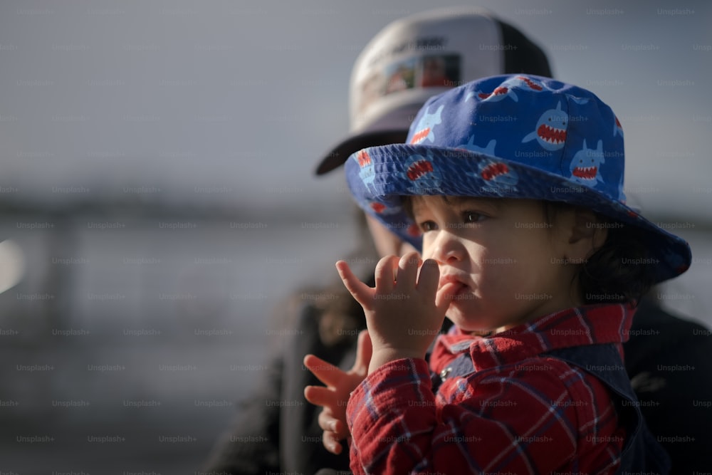 Un niño pequeño con un sombrero azul y haciendo un gesto con la mano