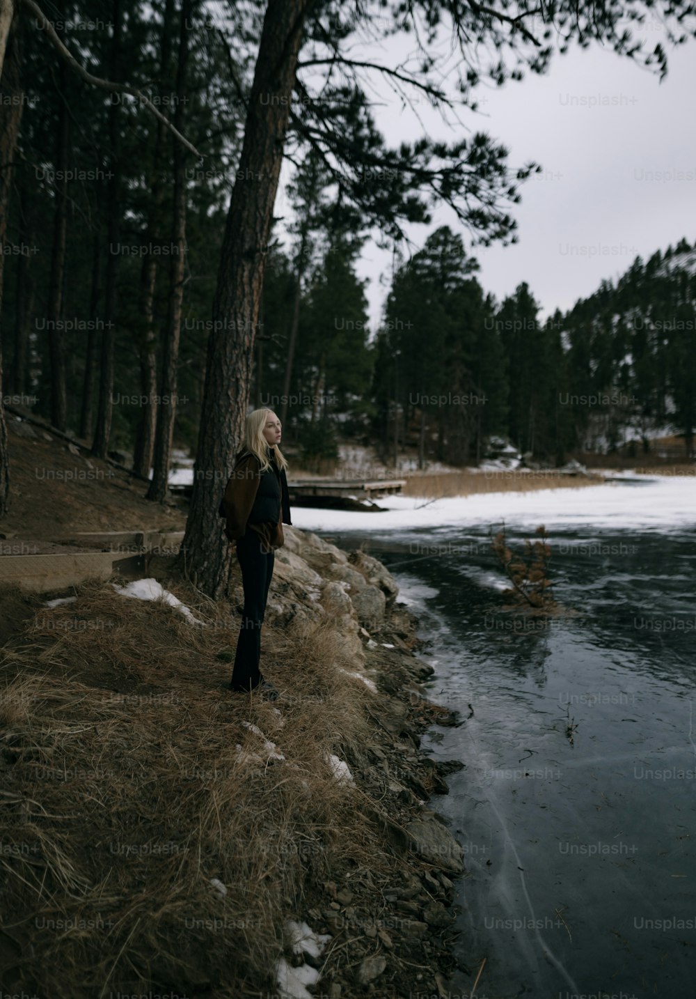 uma mulher de pé ao lado de uma árvore perto de um corpo de água
