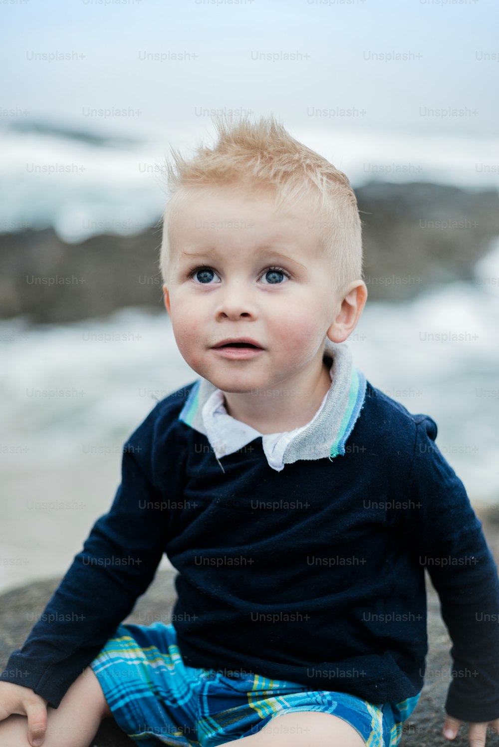 a little boy sitting on a rock near the ocean