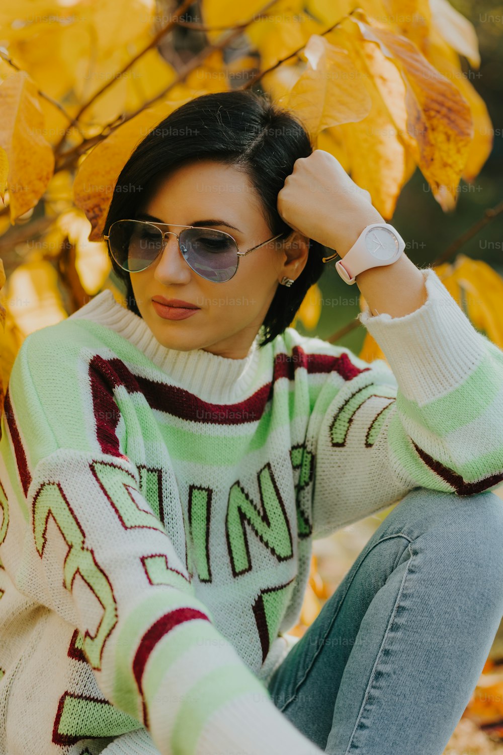 a woman sitting on the ground wearing a sweater and sunglasses