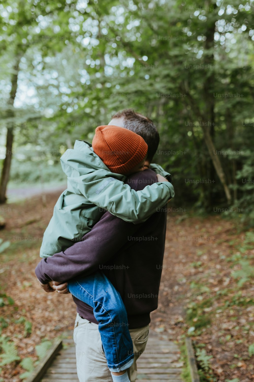 a man carrying a child on a wooden walkway in the woods