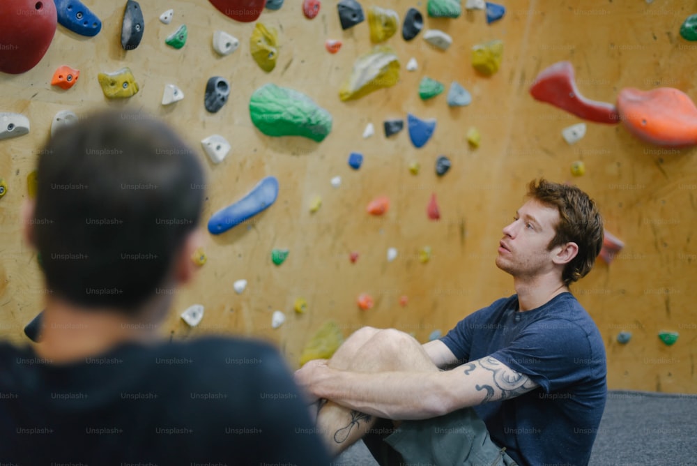 a man sitting in front of a climbing wall