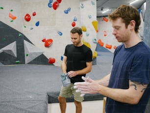 a couple of men standing next to each other near a climbing wall