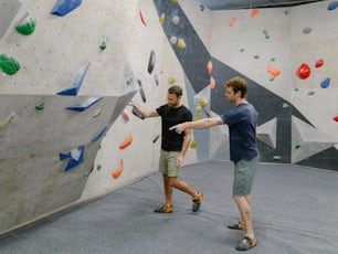 a couple of men standing next to each other near a climbing wall